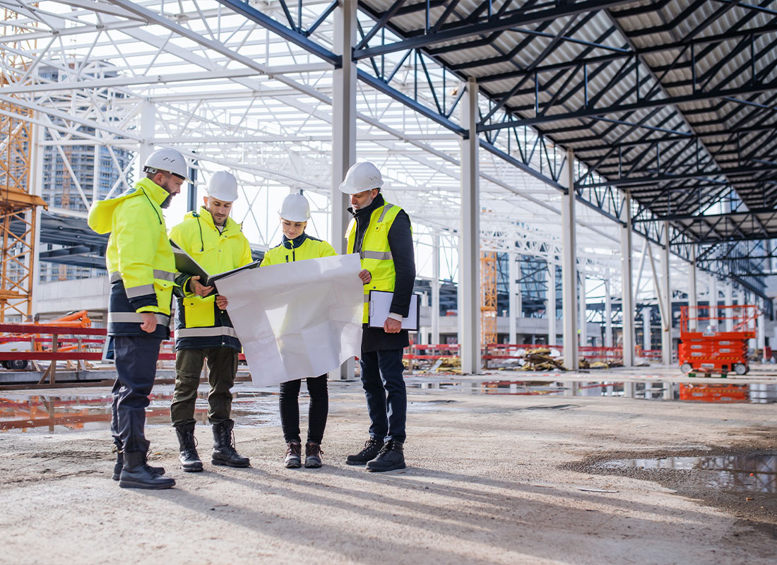Insurance Solutions - Group of Engineers With Blueprints Standing on Construction Site